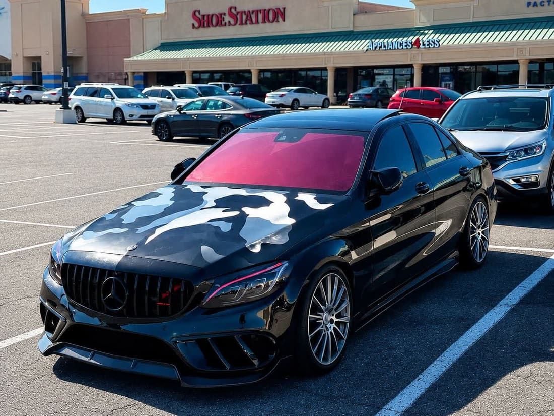 Black Mercedes-AMG sedan with a grey camo hood wrap and tinted red windshield banner